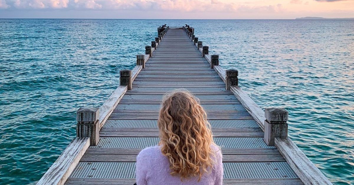 Woman praying on a dock by a lake.
